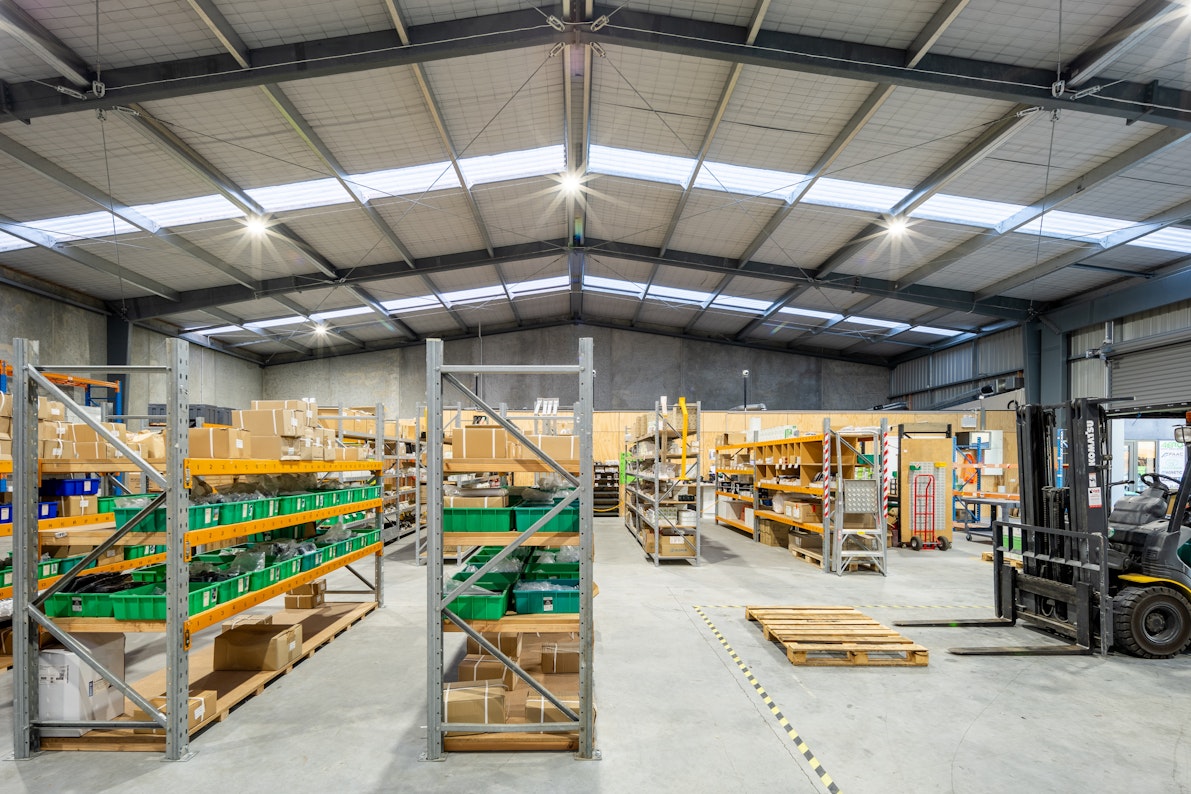 Tidy rows of industrial steel shelving stand inside a large commercial warehouse, with a forklift for packing and organising supplies.